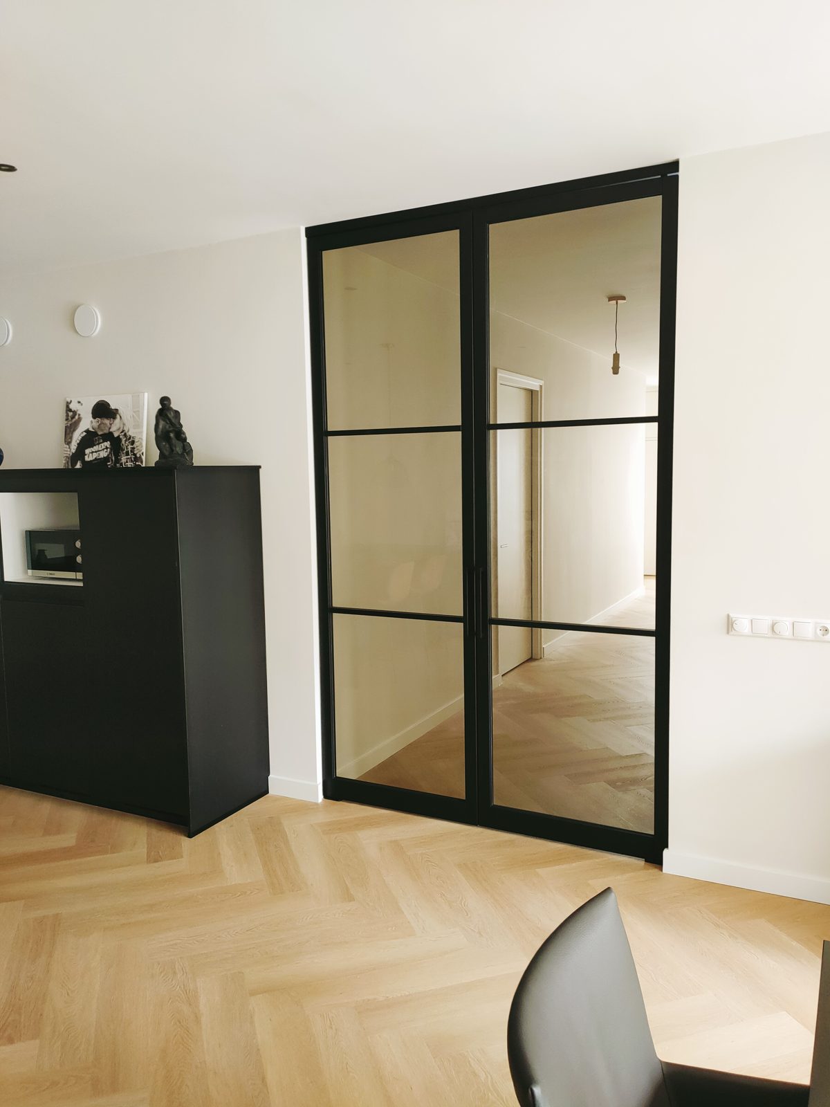 Glazen deur met zwart kader op maat in een woonkamer met visgraatvloer