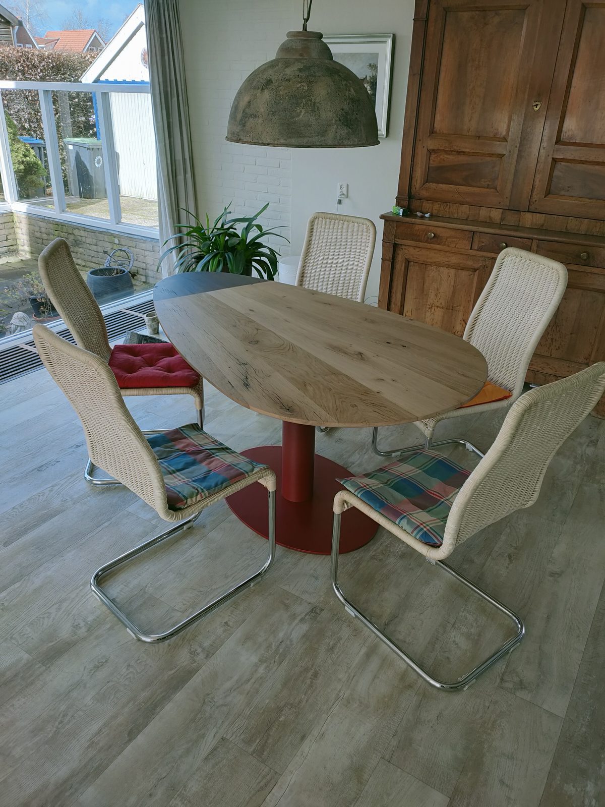 Ronde eiken tafel op maat op een rood metalen voet, met rotan stoelen