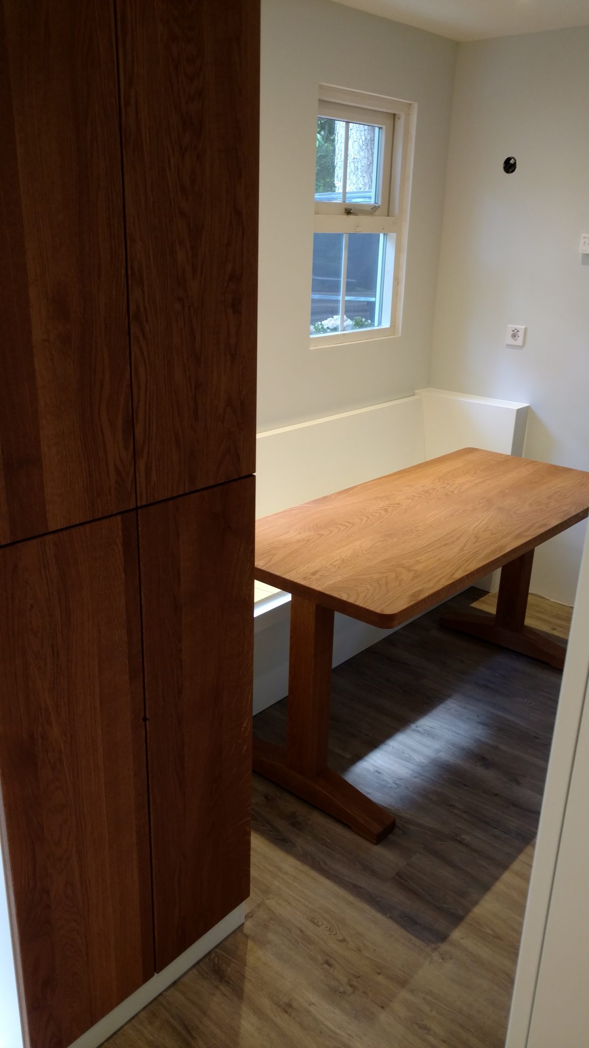 Houten tafel op maat met bank in een nis, naast een donkere houten kast